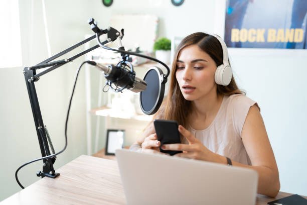 A female podcaster wearing headphones and speaking into a microphone while recording.