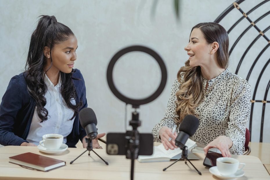 Two women sitting together, recording a podcast using a microphone and ring light.