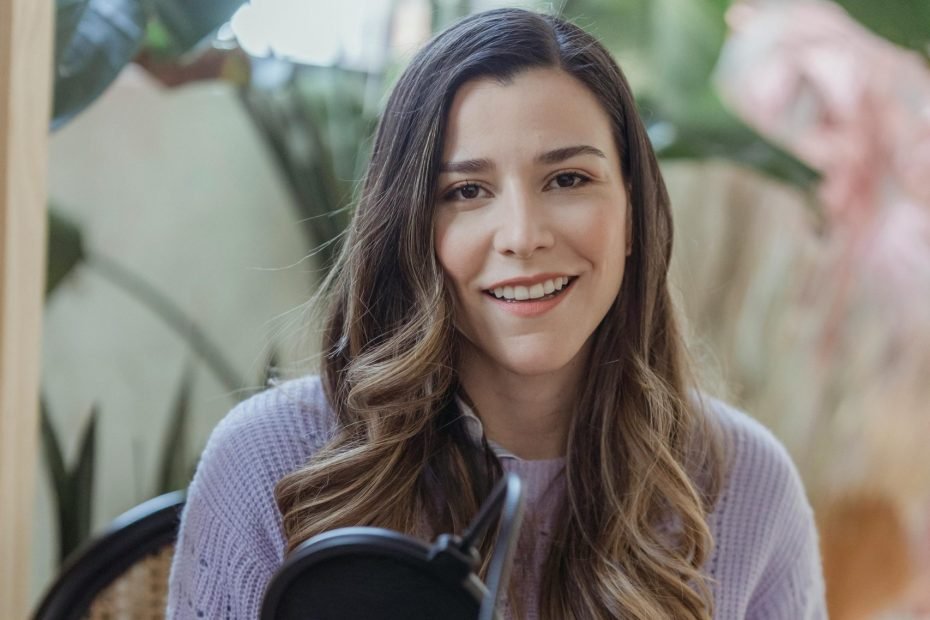 female podcaster with long hair, smiling while speaking into a microphone.