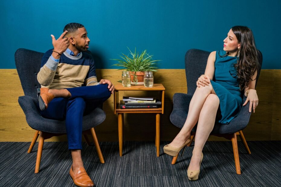 Two peopale seated in chairs, engaging in a podcast interview with microphones.