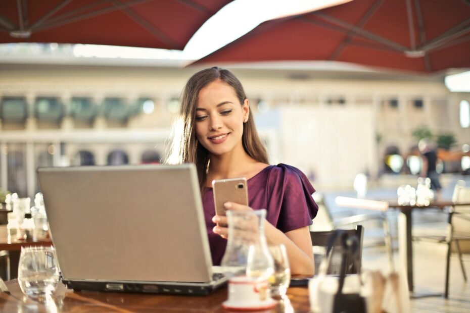 Woman holding mobile and working on laptop