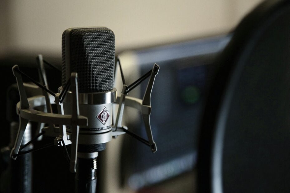 close-up of a studio microphone with pop filter in front of a monitor