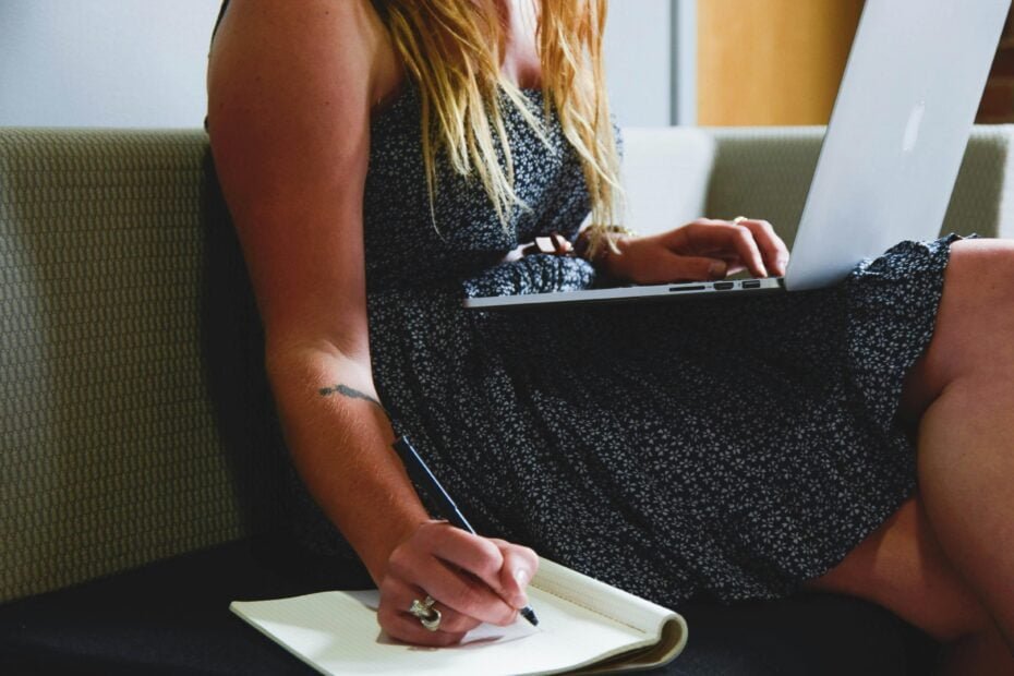 woman writing podcast show notes while sitting next to a laptop