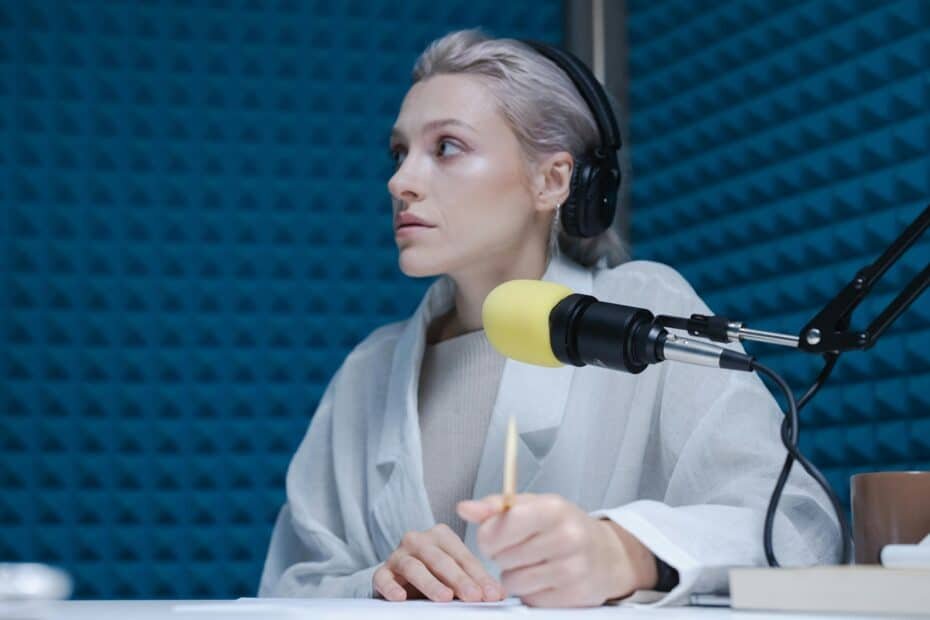 woman podcaster speaking into a microphone with a yellow windscreen with headphones wearing